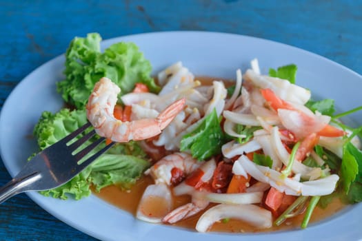 Mixed seafood salad and fork in dish on blue wood table