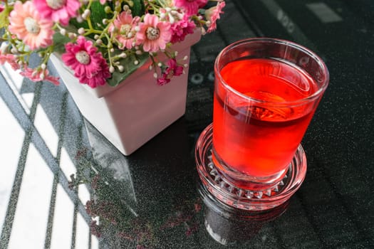 Sweet red water drink in glass and flower on table