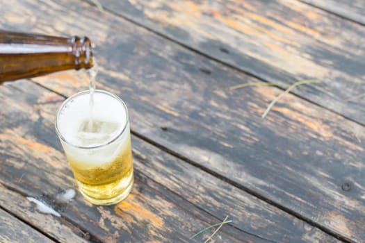 Beer pouring in glass with ice and froth on a wood table