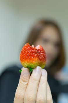 Strawberry with bite holding on asian girl hand, defocus on girl background
