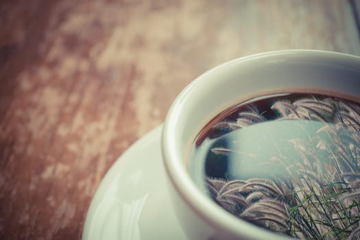 Grass flower (poaceae) reflection on Coffee in white cup on wood table , process in vintage style