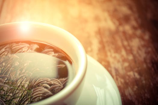 Grass flower (poaceae) reflection on Coffee in white cup on wood table , process in vintage style