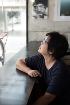 Asian women 40s white skin in black dress with eye glasses have a doubt and think gesture in a coffee shop cafe