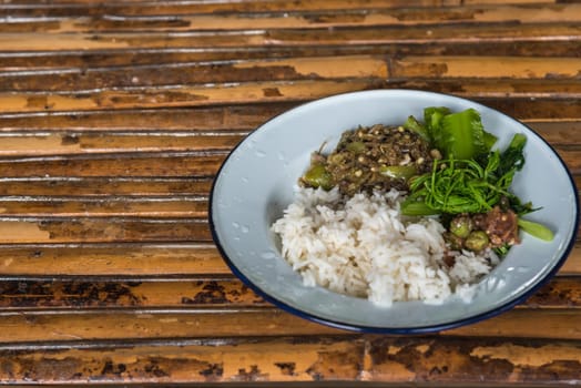 Rice on top with chili sauce or chili paste and traditional vegetable on white dish on a wood table is a local native asian food for sale at Thai street food market or restaurant in Thailand