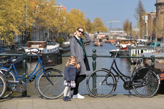 Blonde Dutchwoman mother with her daughter near the bicycle on the bridge over the water channel in Amsterdam city in autumn