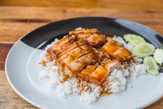 Barbecued red pork in sauce with rice and cucumber served in dish on wood table in Thai restaurant at Thai street food market at Bangkok Thailand