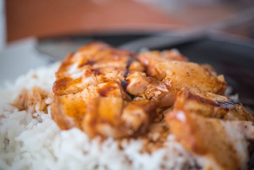Barbecued red pork in sauce with rice and cucumber served in dish on wood table in Thai restaurant at Thai street food market at Bangkok Thailand