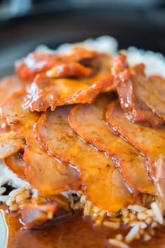 Barbecued red pork in sauce with rice and cucumber served in dish on wood table in Thai restaurant at Thai street food market at Bangkok Thailand