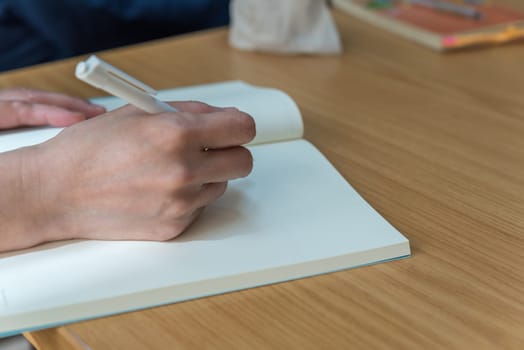 Hand of working or student woman holding a pen for write a message to a book or notebook on a wood table, business or education or journalism concept