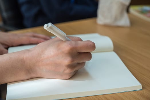 Hand of working or student woman holding a pen for write a message to a book or notebook on a wood table, business or education or journalism concept
