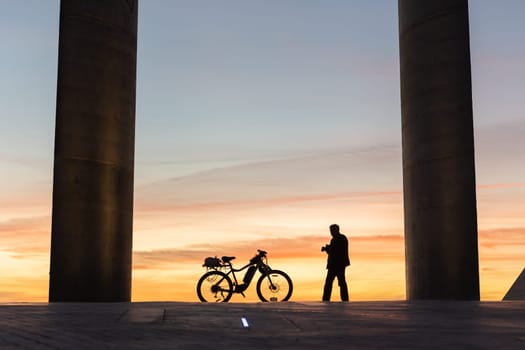 A man walks to his bike on the background of sunset. Mid shot