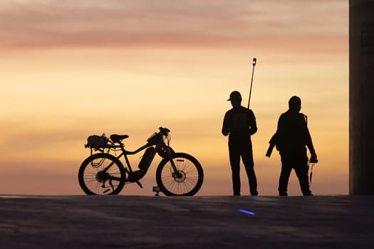 Couple of bloggers standing by a bike at sunset. Mid shot
