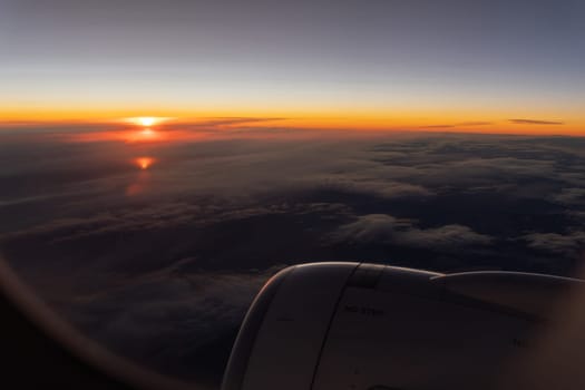 Bright orange sunrise on the horizon over grey clouds. Passenger POV from the plane