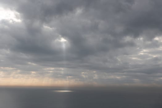 The sun rays breaking through gray clouds reflecting on the sea surface. Mid shot