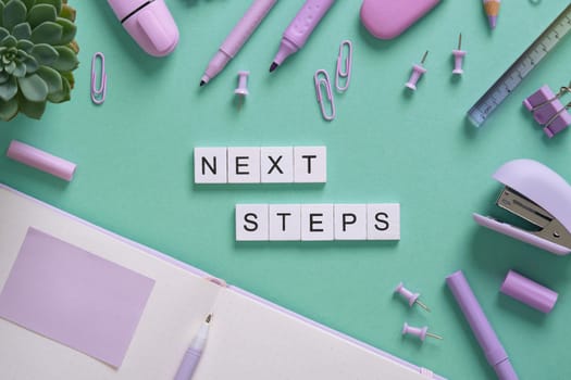 Words Nest Steps in English made of wooden blocks on a background of purple stationery. Mint green backdrop.