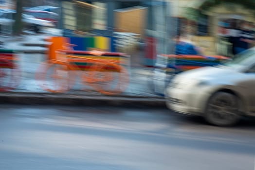 City traffic and road transport is blurred. Bright orange bicycle near cafe and white car.