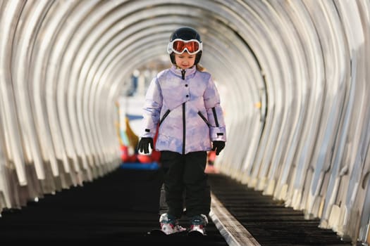 A girl on skis stands on a carpet ski lift in a tunnel