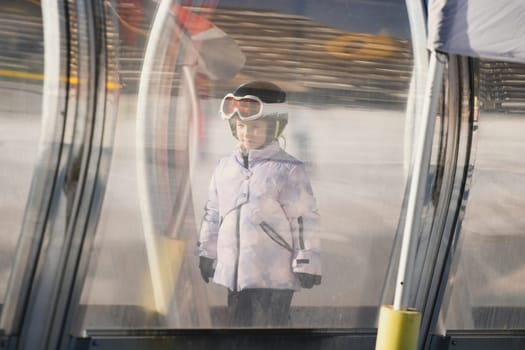 A girl on skis stands on a carpet ski lift in a tunnel