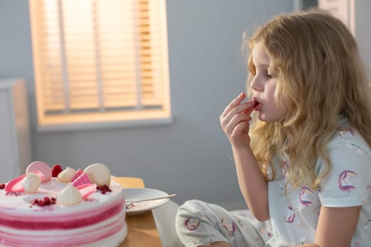 A young girl with curly hair is savoring a delicious slice of cake in a warm and inviting room, enjoying her moment
