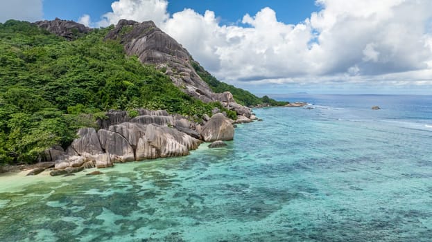Large granite boulders meeting clear ocean waters along a scenic coastline. La Digue, Seychelles.
