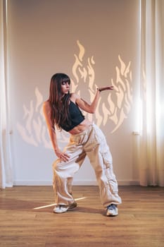 A dancer strikes a dynamic pose in a well-lit studio, showcasing elegant movements. The flames' shadows create a striking visual effect on the wall behind her.