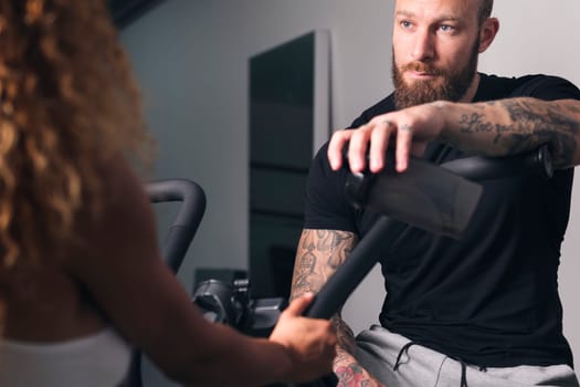 confident muscular bodybuilder with tattoos speaking with anonymous sportswoman at gym, concept of fitness and active lifestyle