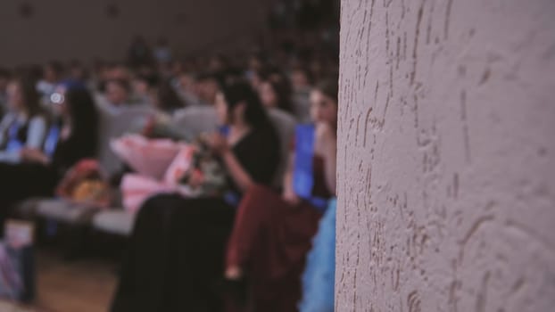 Blurred audience enjoying a graduation ceremony, with a textured wall providing an intriguing backdrop to the celebration of achievement