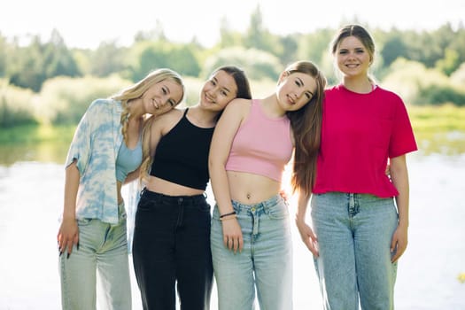 Diverse female friends wearing summer attire, gathering lakeside and sharing laughter during warm outdoor hangout