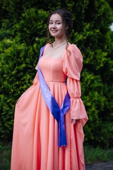 Young woman celebrating her graduation, wearing a sash and an elegant dress, marking a significant milestone in her academic journey
