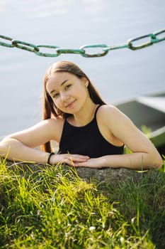 Peaceful teenage girl resting against lakeside rock, basking in warm summer sunlight and tranquil natural scenery