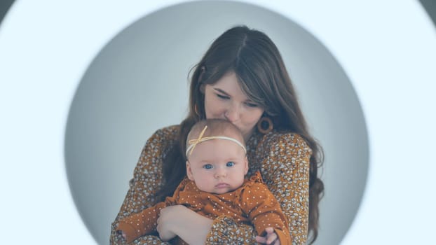 Young mother kissing her baby girl while posing in a circle lighting setup for a cute portrait