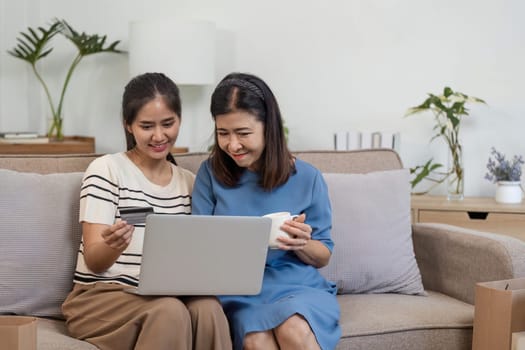 A mother and child happily shop online using a laptop and credit card, enjoying a cozy and modern home setting.