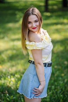 Portrait of a fashionable young woman smiling and posing in a park during a sunny summer day, wearing a denim skirt and a yellow top