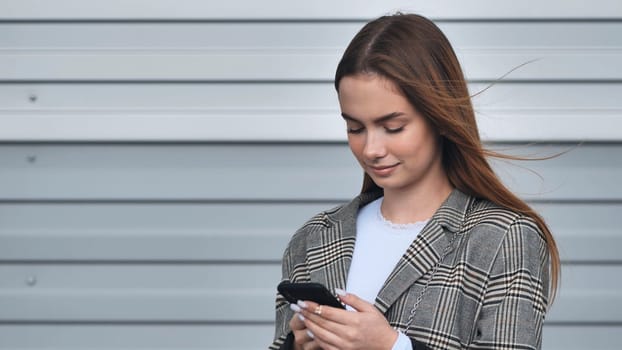 Professional female professional scrolling smartphone screen, networking online near contemporary corporate headquarters during daytime, wearing formal attire