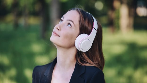 Professional woman listening to music, relaxing on park bench during midday work break, wireless headphones on