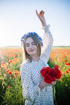 Beautiful blonde woman wearing a cornflower crown holding a bouquet of poppies in a field at sunset, enjoying freedom and nature