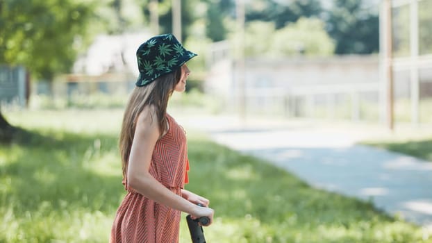 Young woman enjoying a sunny summer day while holding the handlebars of an electric scooter in a vibrant park surrounded by greenery