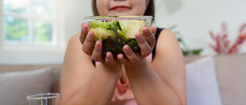 An overweight woman proudly holding a bowl of fresh salad, promoting healthy eating and weight loss in a cozy home atmosphere.