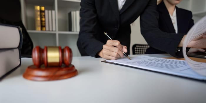 A lawyer carefully signing important legal documents at a desk, with a gavel visible, in a formal office setting.