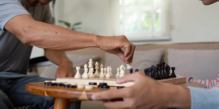 A close-up view of a father skillfully making a chess move while his son attentively observes, showcasing their family bond through shared interests.