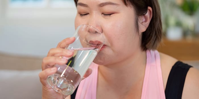 An overweight woman taking a sip of water from a glass at home, emphasizing hydration as part of a healthy lifestyle and weight loss journey.
