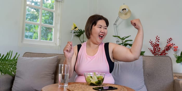 An empowered overweight woman joyfully raising her arms in celebration while enjoying a fresh salad, highlighting healthy weight loss in a vibrant home setting.