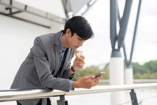 A professional male in a suit eats a snack and checks his phone, illustrating workplace multitasking.