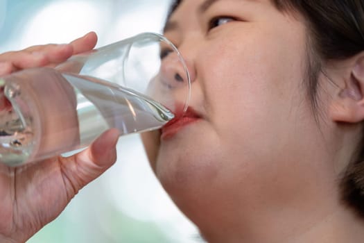 An overweight woman sipping water from a glass, underlining the significance of hydration in her weight loss journey and healthy lifestyle.