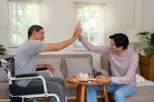 A father and son share a joyful moment, high-fiving after a chess move, showcasing their bond and the happiness of family interactions at home.