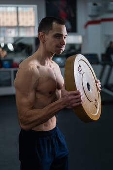 Muscular shirtless man doing exercise with weight plate in gym