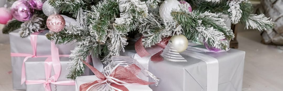 Beautiful decorated Christmas tree with white fireplace and gifts. Christmas tree decorated with toys, balls and lights glowing garlands in living room.