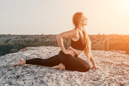 Well looking middle aged woman with long hair, fitness instructor in leggings and tops doing stretching and pilates on the rock near forest. Female fitness yoga routine concept. Healthy lifestyle.