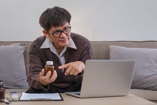 A curious elderly man holds a medicine bottle. Consult with doctor about medication use via video call. Talk to doctor..