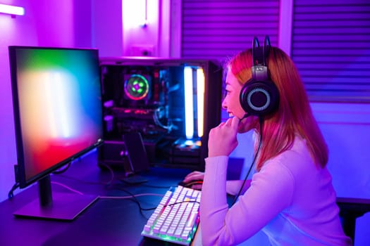 Happy Gamer endeavor plays online video games tournament with computer neon lights, young woman wearing gaming headphones intend to do playing live stream games online at home